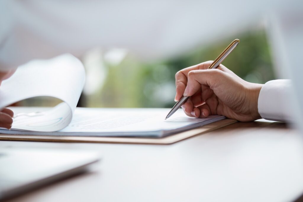 Business Agreement Signing - Close-up of Hand Signing Contract with Pen on Desk