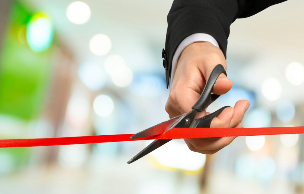 Businessman cutting red ribbon with pair of scissors