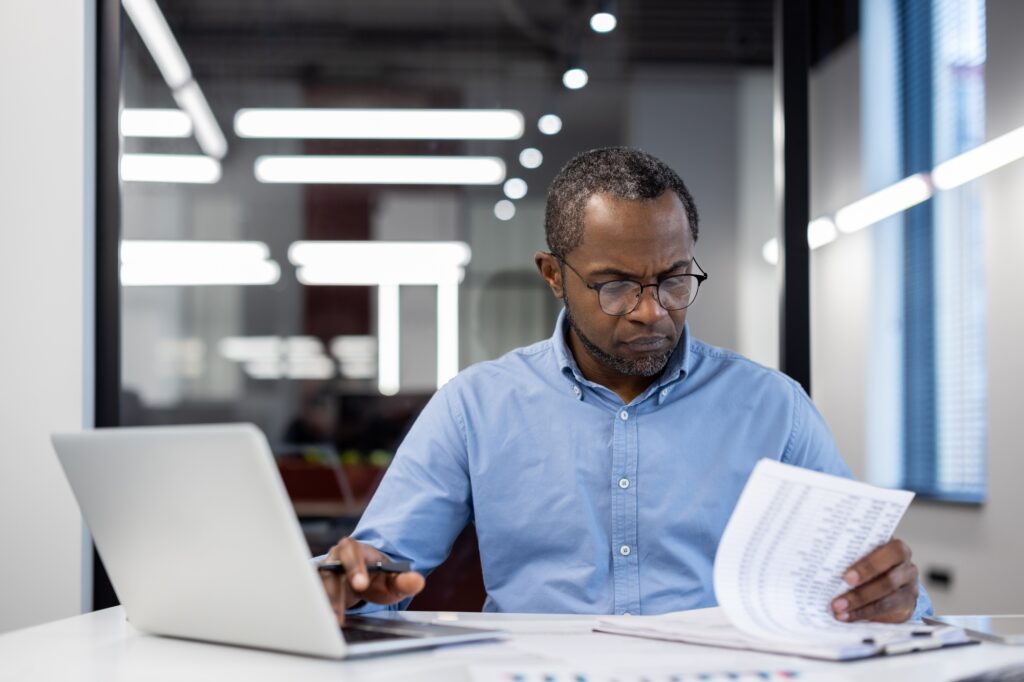 Focused business professional reviewing documents with laptop in modern office environment