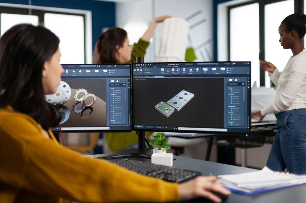 Industrial engineer woman working at pc with two monitors, screens showing CAD software